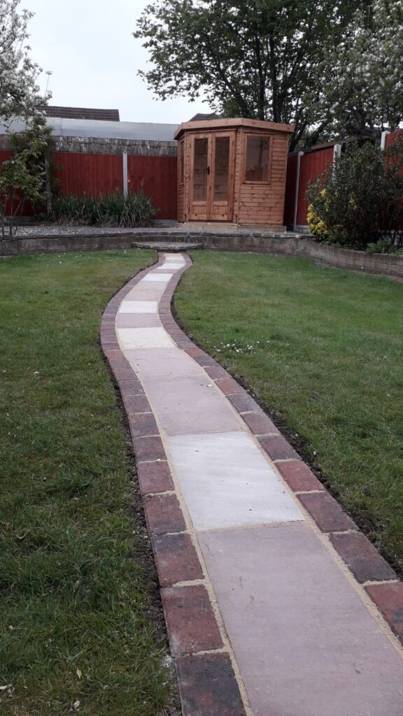 Stone path leading to small corner wooden shed with grass around
